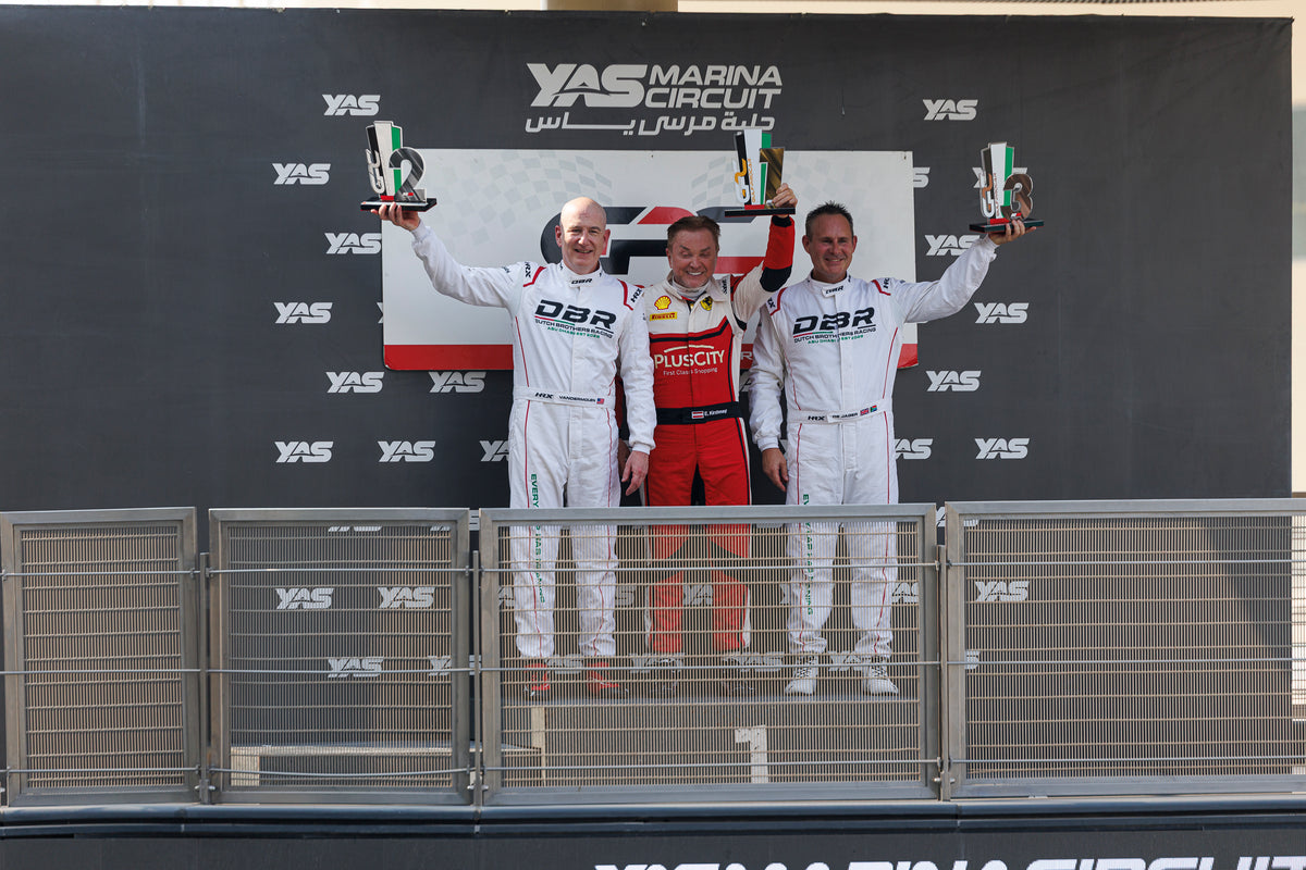 Three drivers on the podium at Yas Marina Circuit holding their trophies, a Dutch Brothers Racing driver in white on either side.