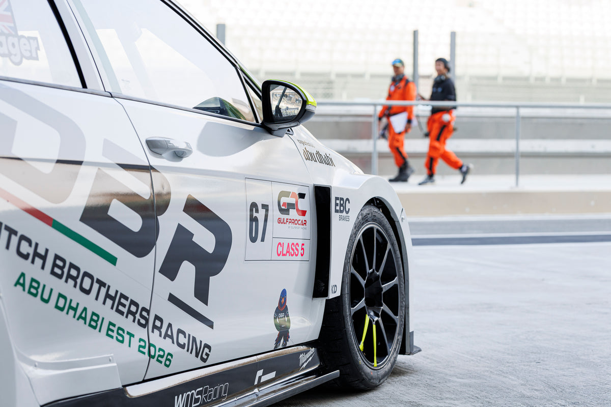 The flank of the number 67 Dutch Brothers Racing Golf, carrying Dutch Brothers Racing, Abu Dhabi Est 2026 and the Class 5 decal, with marshals in orange behind.