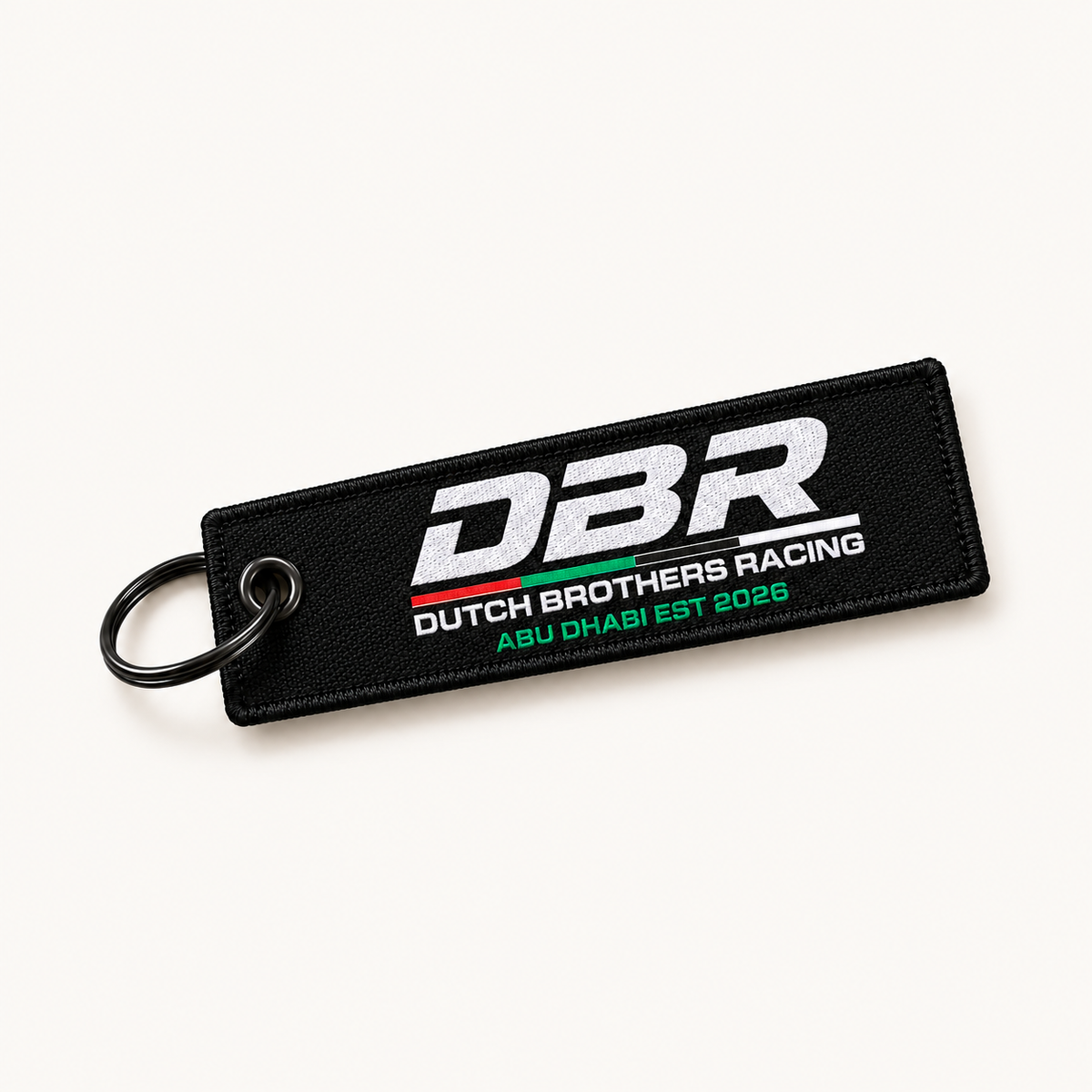 Dutch Brothers Racing keyring, a black woven tag with the DBR logo embroidered in white and Abu Dhabi Est 2026 beneath it, on a black split ring.