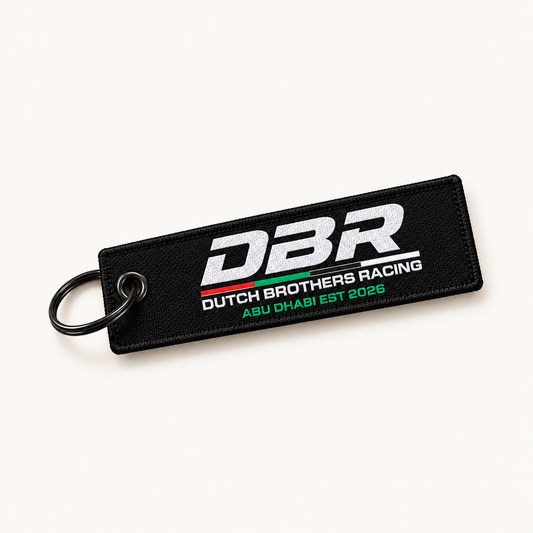 Dutch Brothers Racing keyring, a black woven tag with the DBR logo embroidered in white and Abu Dhabi Est 2026 beneath it, on a black split ring.