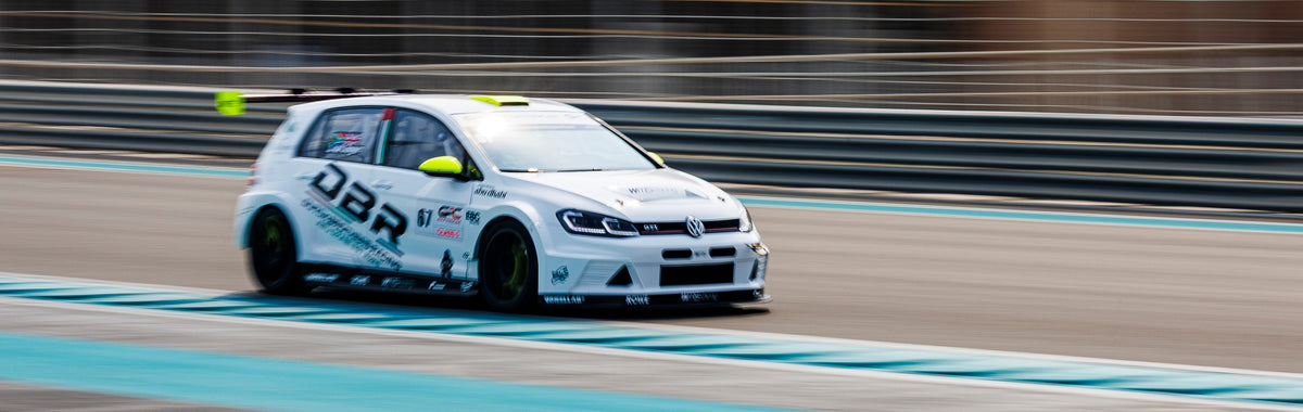 A Dutch Brothers Racing Golf GTI at speed on track at Yas Marina, panned so the barriers behind it blur.