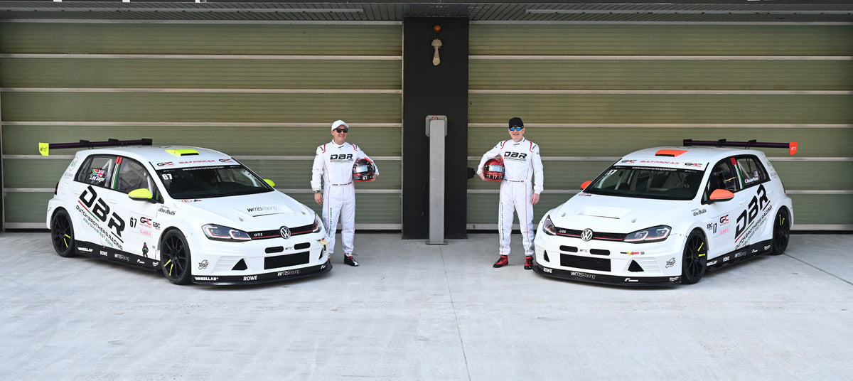 Both Dutch Brothers Racing Golfs parked outside the garage at Yas Marina Circuit, a driver standing beside each car holding his helmet.
